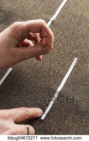 Stock Image - Restoration studio, restorer, hands sewing finished support fabric on lent scarf at paper strip marking, Munich, Bavaria, Germany, Europe. Fotosearch