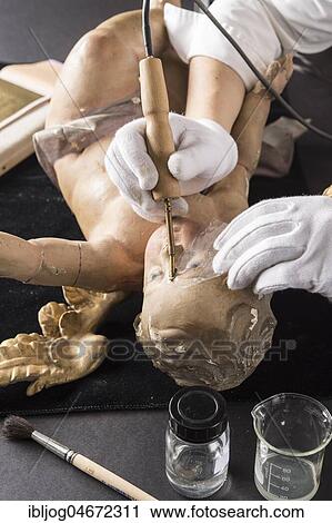 Stock Image - Restoration studio, restorer, hands smoothing glue with heating spatula on angel's face, for fixing the filling material, Munich, Bavaria, Germany, Europe. Fotosearch