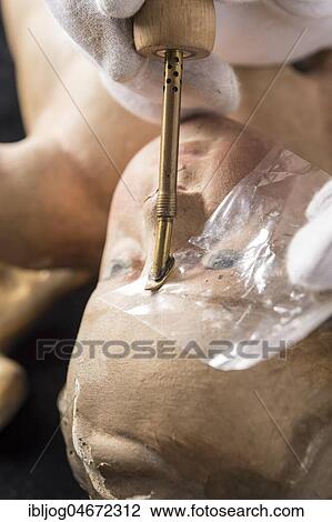 Stock Image - Restoration studio, restorer, hands smoothing glue with heating spatula on angel's face, for fixing the filling material, Munich, Bavaria, Germany, Europe. Fotosearch