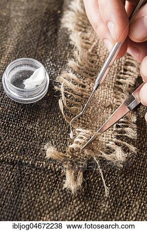 Restoration studio, restorer, hands fixing a linen patch with thread bridge with tools and glue over a crack in a lent scarf, Munich, Bavaria, Germany, Europe View Large Photo Image Stock Photo - Restoration studio, restorer, hands fixing a linen patch with thread bridge with tools and glue over a crack in a lent scarf, Munich, Bavaria, Germany, Europe. Fotosearch