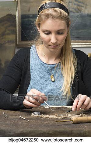 Stock Image - Restoration studio, restorer, woman restores lent scarf with tools on worktable in Atelier, Munich, Bavaria, Germany, Europe. Fotosearch