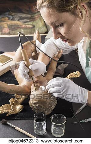 Stock Image - Restoration studio, restorer, woman smoothes glue with heating spatula on the face of an angel, for fixing the filling material, Munich, Bavaria, Germany, Europe. Fotosearch