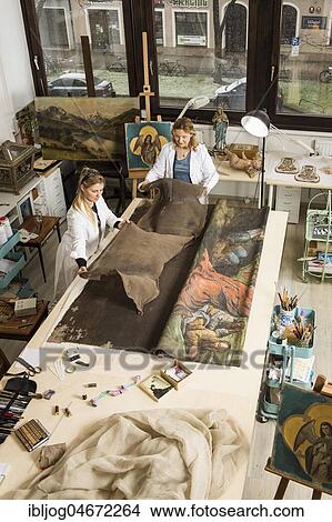 Picture - Restoration studio, restorers, women lay a finished piece of linen for supporting fabric on a worktable with lent scarf in atelier, Munich, Bavaria, Germany.. Fotosearch