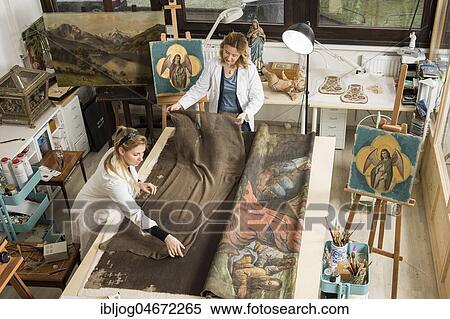 Stock Photography - Restoration studio, restorers, women lay a finished piece of linen for supporting fabric on a worktable with lent scarf in atelier, Munich, Bavaria, Germany.. Fotosearch