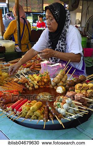 Stock Image - Saleswoman at the market stand with different skewers with meat and seafood, seafood, typical for the country, Naka Weekend Market, Phuket, Thailand, Asia. Fotosearch