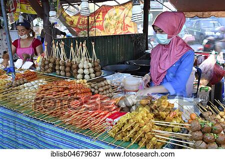 Stock Photo - Saleswoman at the market stand with different skewers with meat and seafood, seafood, typical for the country, Naka Weekend Market, Phuket, Thailand, Asia. Fotosearch