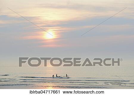 Stock Image - Silhouettes, surfers on the quiet North Sea in the evening, Norderney, East Frisian Islands, Lower Saxony, Germany, Europe. Fotosearch
