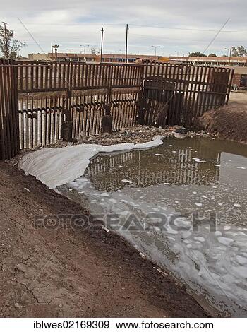 Stock Photo - The heavily-polluted New River, as it enters the USA from Mexico, the pollution results from a mix of untreated sewage, agricultural runoff, and industrial waste; the barrier in the river prevents migrants from using the river to enter the United.... Fotosearch