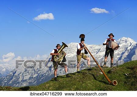 Stock Photo - Three folk musicians play in front of mountain panorama, Bergfexn trio in traditional costume on the Eggenalm, behind Loferer Steinberge, Reit im Winkl, Bavaria, Upper Bavaria, Germany, Europe. Fotosearch