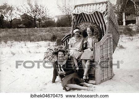 Stock Photography - Three women on the beach, two sitting in beach chairs with sunshades, vacation 1920s, Baltic Sea, Germany, Europe. Fotosearch