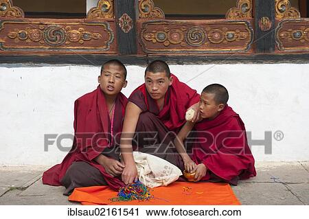 Stock Image - Tibetan Buddhism, three novices sitting on the ground wearing red robes, Rinpung Dzong Monastery and Fortress, courtyard, Paro, Himalayas, Bhutan, South Asia, Asia. Fotosearch
