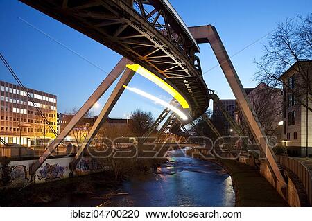Stock Image - Trail of light from a moving suspension railway above the Wupper, Wuppertal, Bergisches Land, North Rhine-Westphalia, Germany, Europe. Fotosearch