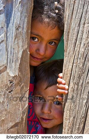 Stock Image - Two young boys peering curiously through a gap in a wooden wall, Middle Atlas, Morocco, Africa. Fotosearch