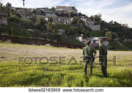 Stock Photo - U. S. Border Patrol agents north of the international border fence between the United States and Mexico, Tijuana neighborhood on the hill beyond the fence, San Ysidro, California, USA, North America. Fotosearch