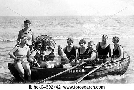 Stock Image - Vacation, nine women in swimsuit and with big champagne bottle on the beach in a rowing boat, group photo, 1920s, Baltic Sea, Rügen, Germany, Europe. Fotosearch