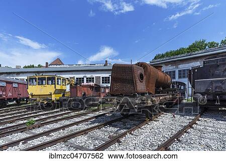Stock Image - Various locomotives and a rusty hull of a steam locomotive in front of a roundhouse, Bavarian Railway Museum Nördlingen, Nördlingen, Bavaria, Germany, Europe. Fotosearch