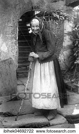 Stock Image - Wood collector, old woman wearing a basket full of firewood, 1920s, Germany, Europe. Fotosearch