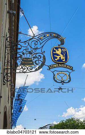 Stock Image - Wrought iron shop sign and flags, Löwenbräukeller at Stiglmaierplatz, Munich, Upper Bavaria, Bavaria, Germany, Europe. Fotosearch