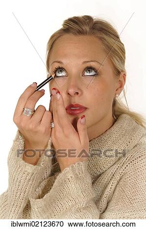 Stock Image - Young woman applying make-up, eyeliner. Fotosearch