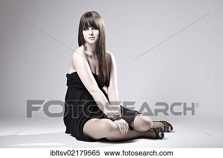 Stock Photography - Young woman posing in black dress, sitting. Fotosearch