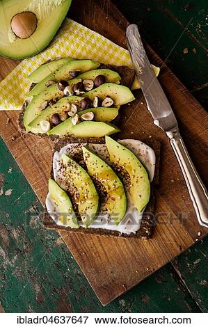 Stock Photo - Black bread with curd cheese, avocado and nuts, food still-life, studio shot. Fotosearch