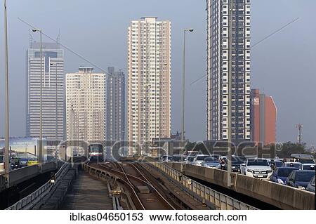 Stock Image - BTS Skytrain drives next to a motorcade, morning traffic jam on Saphan Taksin Bridge, Bangkok, Thailand, Asia. Fotosearch