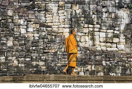 Buddhist monk walks in front of old stone wall, Bayon temple, temple ruin, temple complex, Angkor Wat, Angkor Archaeological Park, Siem Reap Province, Cambodia, Asia View Large Photo Image Stock Photo - Buddhist monk walks in front of old stone wall, Bayon temple, temple ruin, temple complex, Angkor Wat, Angkor Archaeological Park, Siem Reap Province, Cambodia, Asia. Fotosearch