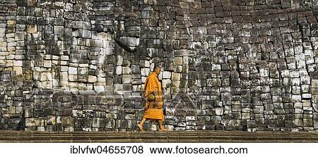 Buddhist monk walks in front of old stone wall, Bayon temple, temple ruin, temple complex, Angkor Wat, Angkor Archaeological Park, Siem Reap Province, Cambodia, Asia View Large Photo Image Stock Photo - Buddhist monk walks in front of old stone wall, Bayon temple, temple ruin, temple complex, Angkor Wat, Angkor Archaeological Park, Siem Reap Province, Cambodia, Asia. Fotosearch