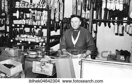 Picture - Butchery, saleswoman stands behind shop counter, 1960s, Germany, Europe. Fotosearch