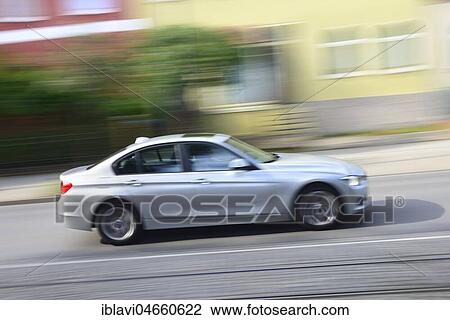Stock Image - Car 3 Series BMW drives through residential area, motion blur, Germany, Europe. Fotosearch