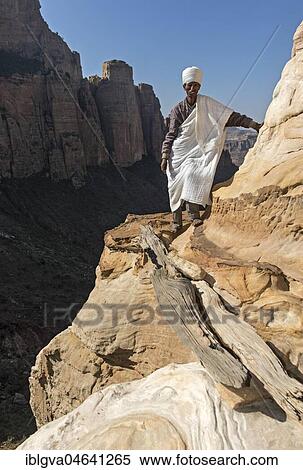 Stock Photography - Coptic priest on a rock ledge at the entrance to Abuna Yemata monolithic church, Gheralta Region, Tigray, Ethiopia, Africa. Fotosearch