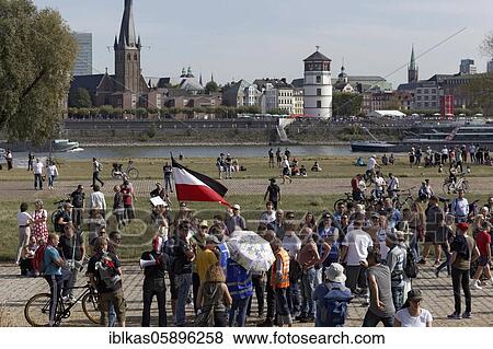 Stock Photo - Demo against Corona rules on the Rhine meadows, man with forbidden Reich war flag, surrounded by people, Düsseldorf, North Rhine-Westphalia, Germany, Europe. Fotosearch