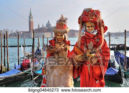 Stock Image - Disguised couple with Venetian masks at the lagoon, behind island San Giorgio, carnival in Venice, Italy, Europe. Fotosearch