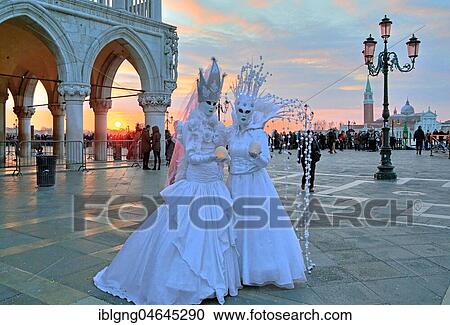 Stock Image - Disguised couple with Venetian masks at sunset, behind island of San Giorgio, carnival in Venice, Italy, Europe. Fotosearch