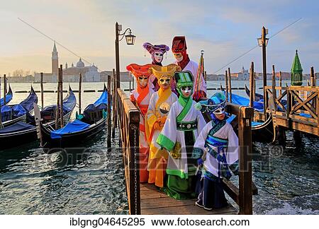 Stock Photography - Disguised persons with Venetian masks on walkway at the lagoon, behind island of San Giorgio, carnival in Venice, Italy, Europe. Fotosearch