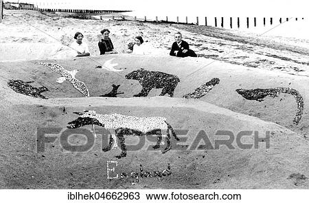 Stock Image - Family on a sandy beach with sandcastle, 1930s, England. Fotosearch