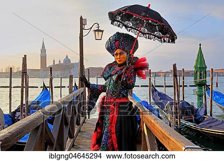 Picture - Female disguised with Venetian mask on walkway at the lagoon, behind island of San Giorgio, carnival in Venice, Italy, Europe. Fotosearch