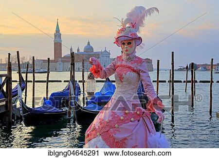 Stock Image - Female disguised with Venetian mask on the lagoon, behind island of San Giorgio, carnival in Venice, Italy, Europe. Fotosearch