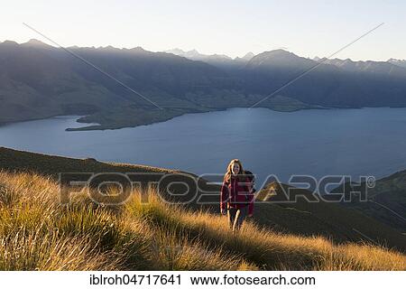 Stock Image - Female hiker at Isthmus Peak, Lake Wanaka and mountain panorama at atmospheric evening light, Otago, South Island, New Zealand, Oceania. Fotosearch