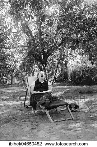 Stock Image - Grandma yawns in a deck chair in the garden, 1930s, Germany, Europe. Fotosearch