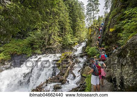 Stock Image - Hikers on the alpine path through the Höllschlucht gorge with waterfall, theme trail Wild Waters, Rohrmoos-Untertal, Schladminger Tauern, Schladming, Styria, Austria, Europe. Fotosearch