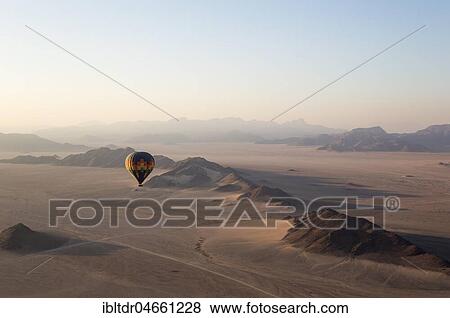 Hot-air balloon above an arid plain and isolated mountain ridges, at dawn, Namib Desert, aerial view from a second balloon, NamibRand Nature Reserve, Namibia, Africa View Large Photo Image Stock Photo - Hot-air balloon above an arid plain and isolated mountain ridges, at dawn, Namib Desert, aerial view from a second balloon, NamibRand Nature Reserve, Namibia, Africa. Fotosearch