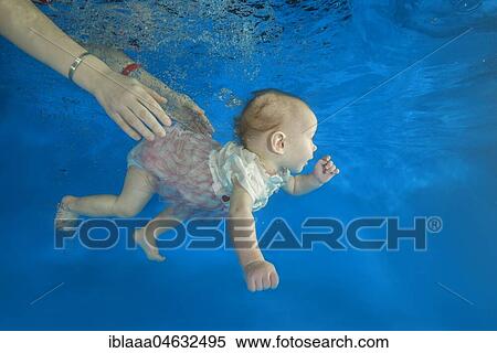 Infant girl dives in a pool with hands of her mother holding it View Large Photo Image Stock Photography - Infant girl dives in a pool with hands of her mother holding it. Fotosearch