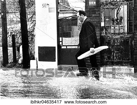 Stock Photo - Man carrying a baguette through a flooded street, between 50s and 60s, exact location unknown, France, Europe. Fotosearch