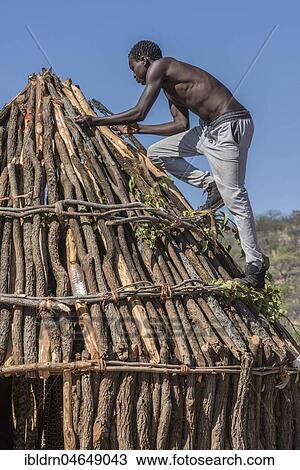 Stock Image - Man of the people of Ovahimba or Himba builds on the roof of a wooden hut, Kunene district, Namibia, Africa. Fotosearch