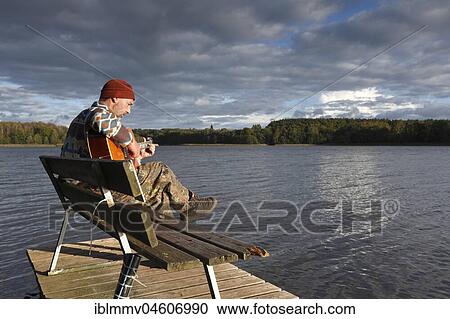 Man plays guitar on a boat landing stage at the lake, Mecklenburg Lake District, Mecklenburg-Western Pomerania, Germany, Europe View Large Photo Image Stock Image - Man plays guitar on a boat landing stage at the lake, Mecklenburg Lake District, Mecklenburg-Western Pomerania, Germany, Europe. Fotosearch