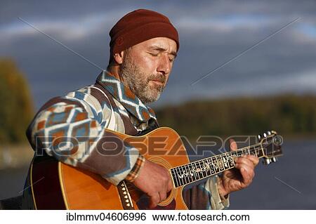 Stock Photograph - Man plays guitar on a boat landing stage at the lake, Mecklenburg Lake District, Mecklenburg-Western Pomerania, Germany, Europe. Fotosearch