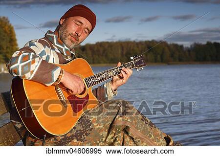 Stock Photography - Man plays guitar on a boat landing stage at the lake, Mecklenburg Lake District, Mecklenburg-Western Pomerania, Germany, Europe. Fotosearch