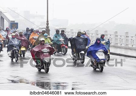 Stock Image - Mopeds on street during rain, trafffic on the Trang Tien bridge, Hue, Vietnam, Asia. Fotosearch