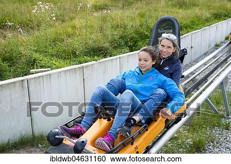 Stock Image - Mother and daughter enjoying a ride with the Alpine Coaster, summer toboggan run at the Kolbensattelhütte near Oberammergau, Upper Bavaria, Bavaria, Germany, Europe. Fotosearch